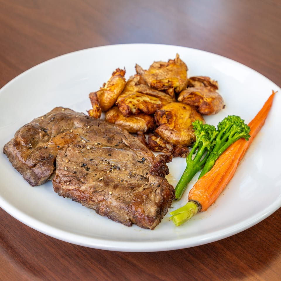 Grilled steak with roasted potatoes, broccoli, and a whole carrot on a white plate.