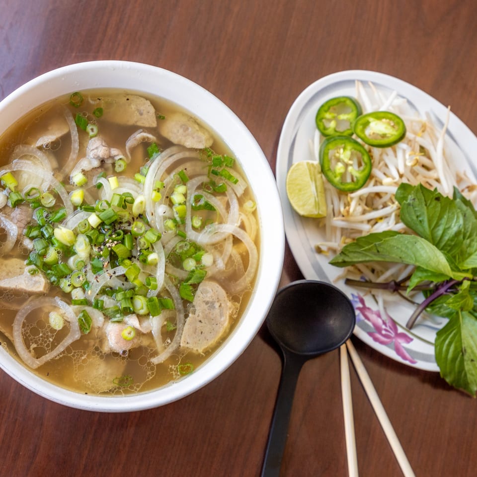 A bowl of Sunset Phở Caffe's Vietnamese pho with a side of fresh herbs and jalapeños.